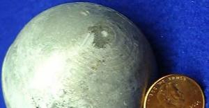A small ball of cadmium metal, with a coin for size reference.